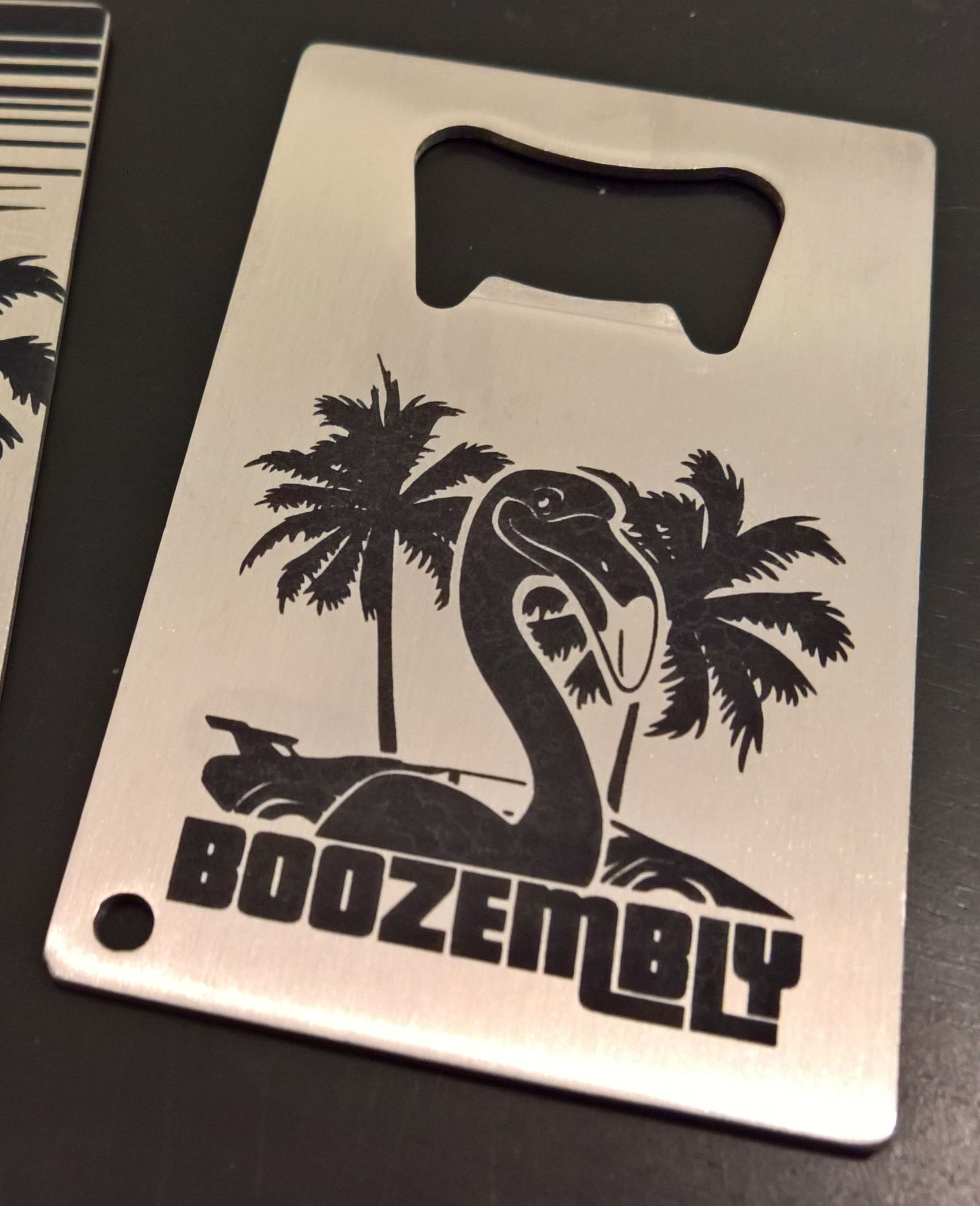 A stainless steel bottle opener that says 'Boozembly'